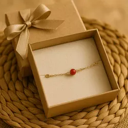 Bracelet corail rouge dans un petit écrin kraft avec ruban, fond naturel