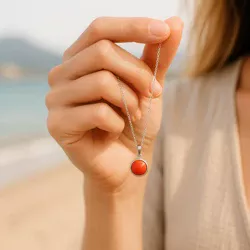 Main féminine tenant un pendentif en corail rouge devant la mer